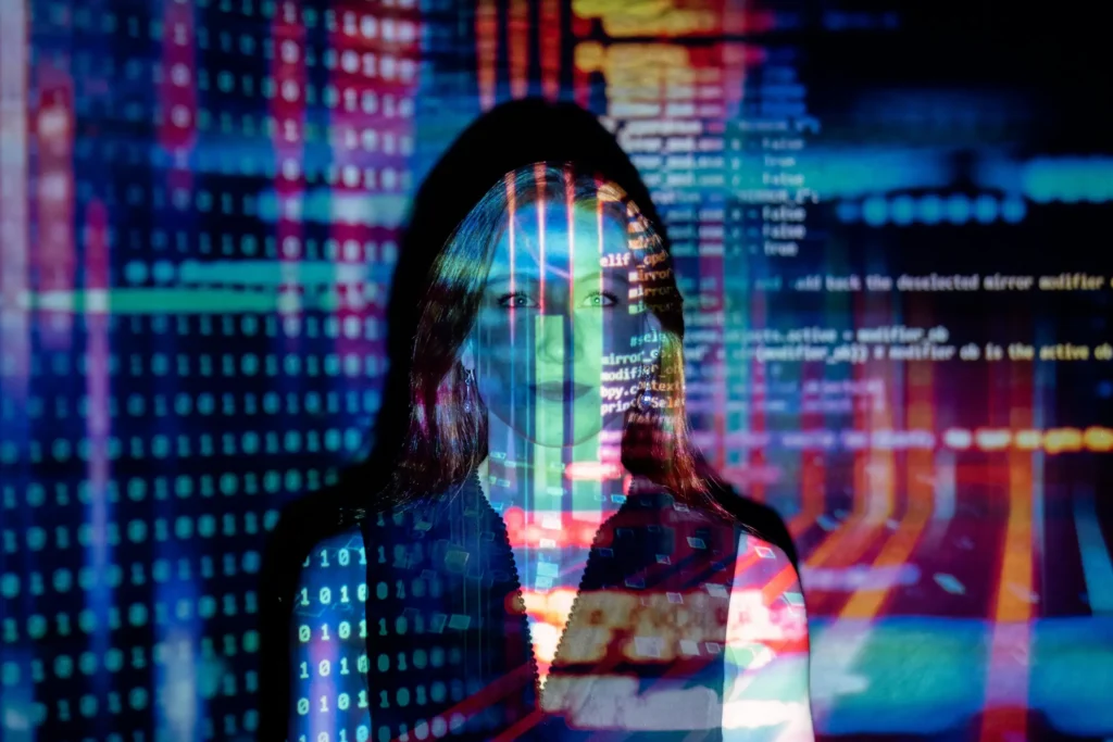 A woman stands facing the camera. Large amounts of data in the form of numbers are letters are projected onto her and the wall behind her. It gives both a futuristic feel and a feeling of an overwhelming amount of information. 