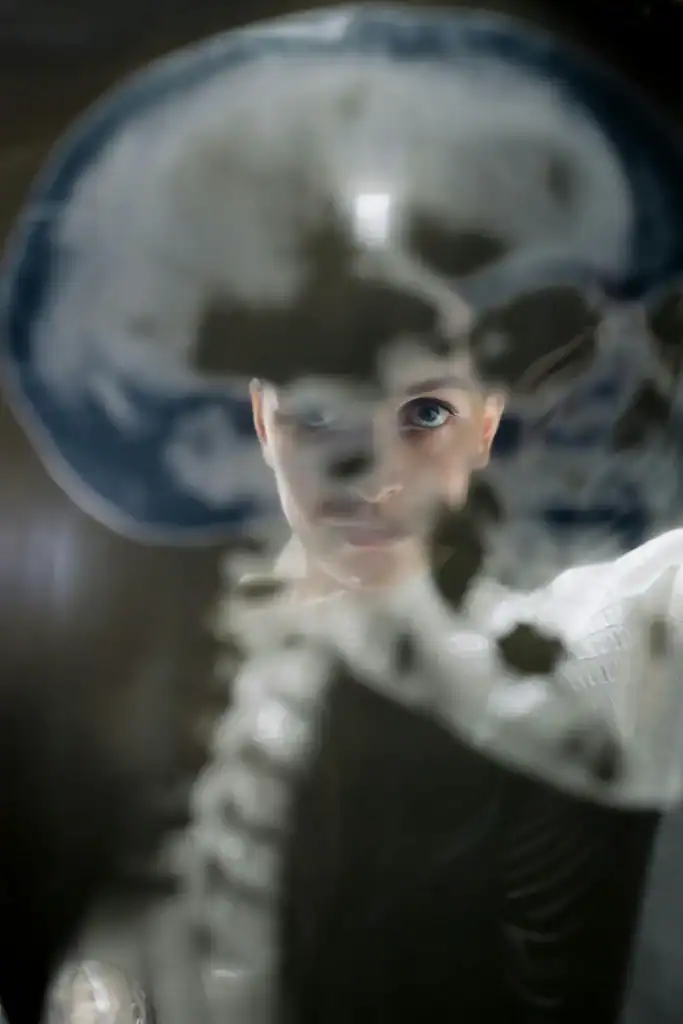 A female doctor holds x-ray image of a human skull up towards the camera. She is looking through it to the camera. 