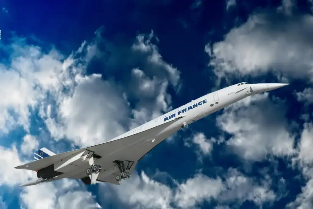 Concorde flies through a blue sky with white fluffy clouds. The words 'Air France' can be read in blue words on the side of the white plane.