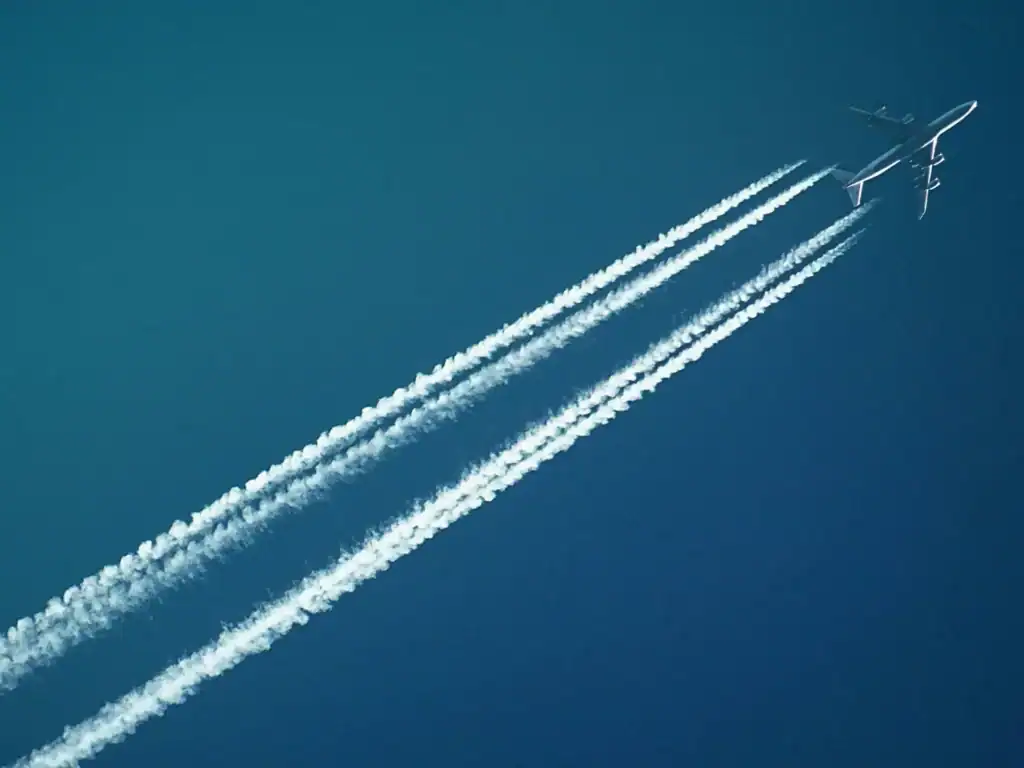 A plane speeds through a blue sky. Four white contrails extend behind the plane, giving the impression of movement.