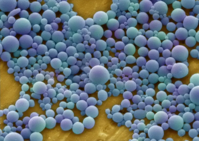 A microscopic iamge of the nanoparticles. Thez are coloured various shades of blue and purple. various siye of nanoparticles can be seen looking like colourful beads