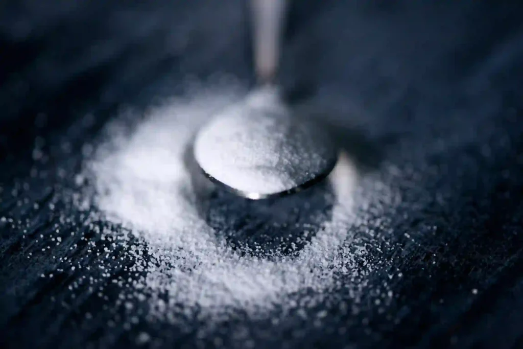 a metal spoon holds sugar, sugar can also be seen scattered on the table.